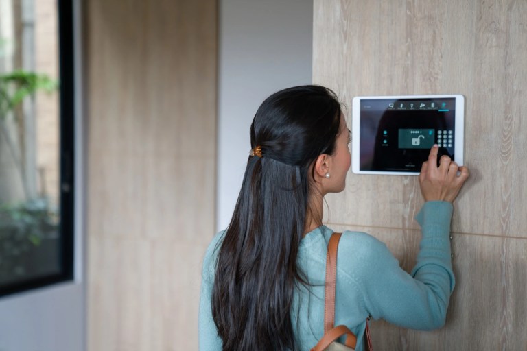 Woman entering a code on a wall-mounted home security panel before leaving