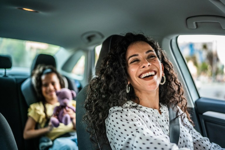 Woman laughing in the driver's seat with a child in a car seat behind