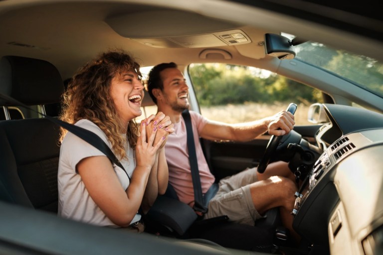 Couple laughing in a car with the man driving and the window down
