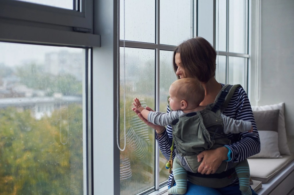 Woman holding a baby at a window streaked with rain