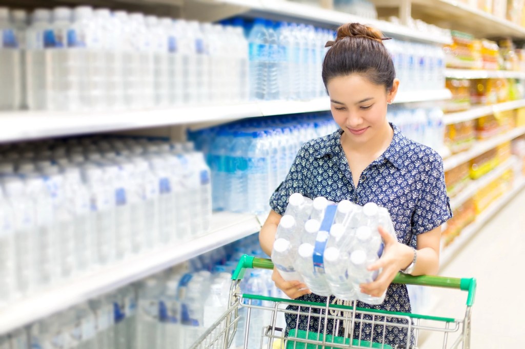 Woman choosing a pack of bottled water in a supermarket aisle