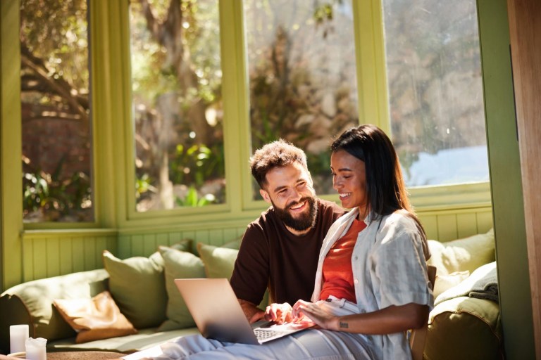 Couple looking at a laptop together on a sunlit window seat